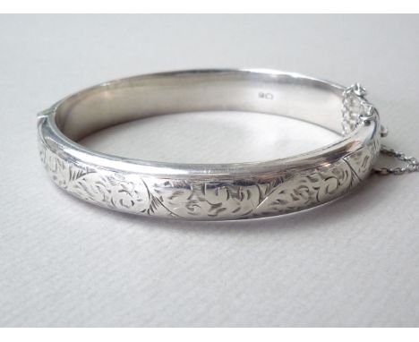A 1960s silver hinged bangle, with patented extension clasp, of hollow shallow D section, the face bright-cut engraved with f
