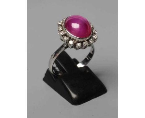 A STAR RUBY AND DIAMOND RING, the oval cabochon ruby collet set to a border of sixteen small diamonds to plain shoulders and 