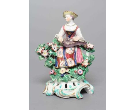 A BOW PORCELAIN FIGURE, c.1760, modelled as Columbine, seated and wearing colourful clothing, playing a hurdy-gurdy, with boc