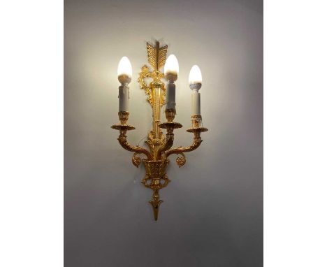 A SET OF FOUR GILT METAL THREE FLAME WALL LIGHTS, 20th century, the wall plate in the form of an arrow issuing three acanthus