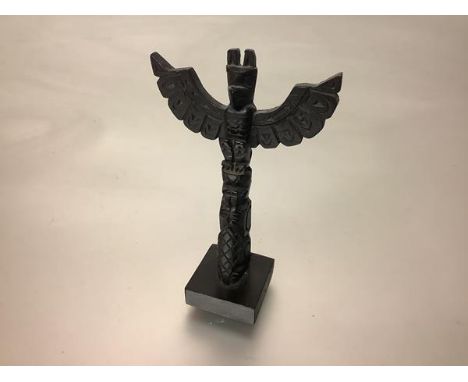 A Native American carved wooden model totem pole, with stylised eagle surmount, on a square wooden base bearing incised initi