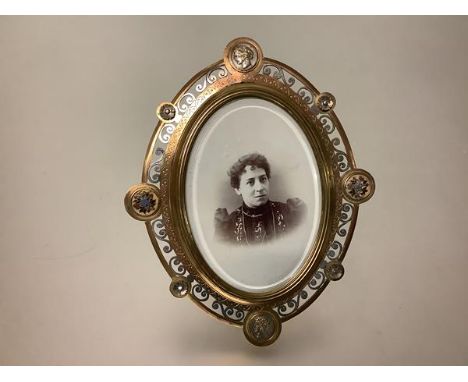 A late 19th century, enamelled, gilt and silvered-brass photograph frame, oval, probably French, the pierced scroll-cast fram