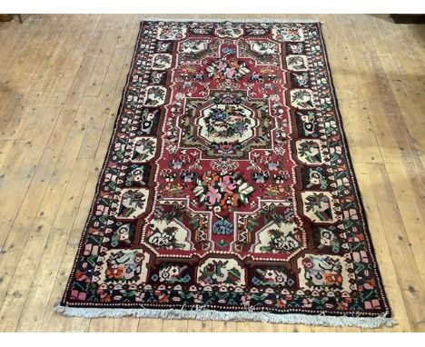 A Bakhtiari hand-knotted wool small carpet, the raspberry-sorbet field with central medallion enclosing flowers, within a til