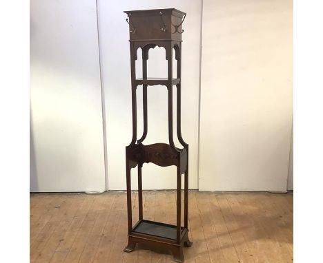 An Edwardian hat and coat stand, the projecting top and frieze applied with brass hooks, above a single shelf and sprung bras