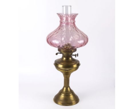 A brass oil lamp with cranberry glass shade