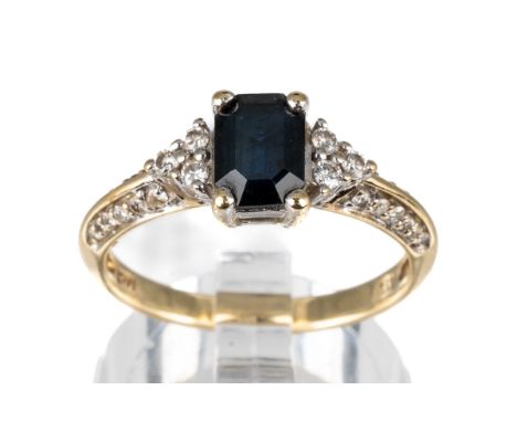 A 10k yellow gold sapphire and diamond ring, set with an emerald-cut sapphire flanked by six diamonds, diamond set shoulders,