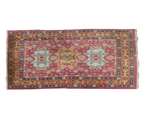 A Chinese carpet, 20th century, probably from Xinjiang province, with shaped panels of stylised ruyi heads against a cranberr