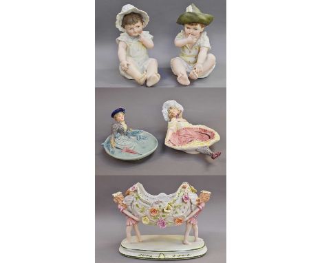 A Pair of German Coloured Bisque Figures of Seated Babies, late 19th century, together with a pair of novelty erotic faience 
