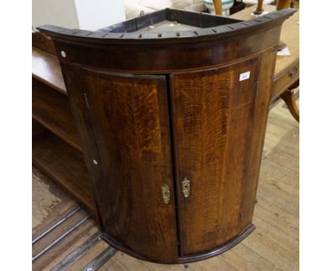 A Georgian inlaid light oak bowfront corner cupboard, the twin panel doors enclosing fixed shelves.