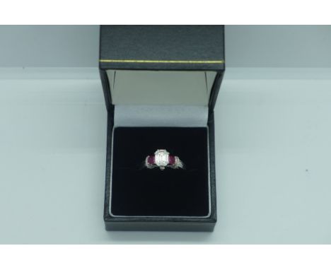 An 18ct white gold ruby and diamond trilogy ring with diamond set shoulders, ring size N, approx 5 grams, emerald cut diamond