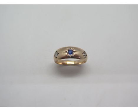 A 9ct pale rose gold diamond and sapphire gypsy ring set with a central sapphire flanked by two old cut diamonds ring, size L