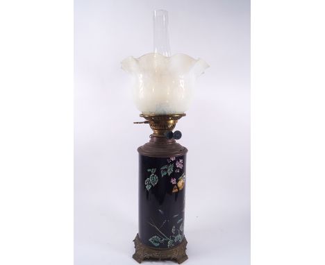 A Victorian oil lamp the cylindrical earthenware body painted with flowers on a blue ground, with brass mounts and etched opa