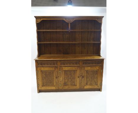 A modern oak dresser with carved oakleaf detail, the two shelf plate rack over three drawers with turned acorn handles and pa