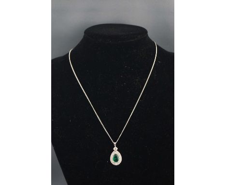 A white metal cluster pendant centrally set with a pear faceted cut emerald, estimated to weigh 1.06 carats. Further set with