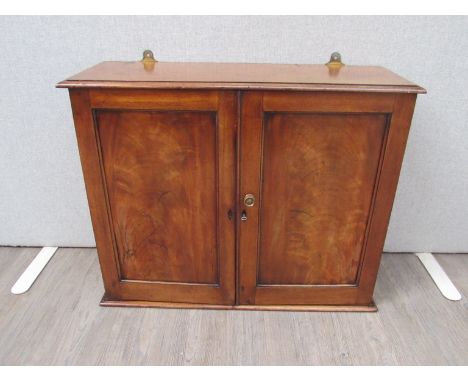 Circa 1840 a flame mahogany wall hanging two door cupboard with key opening to reveal a three drawer and shelf interior