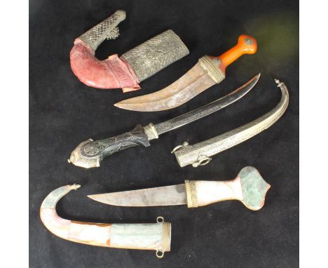 Three assorted Jambiya daggers, one with agate mounted grip and scabbard and brass detailing, another with amber style grip a