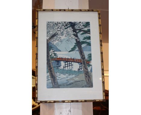 A Japanese woodcut print depicting figures on a bridge, mountains beyond, with character marks, 35.5cm by 23.5cm