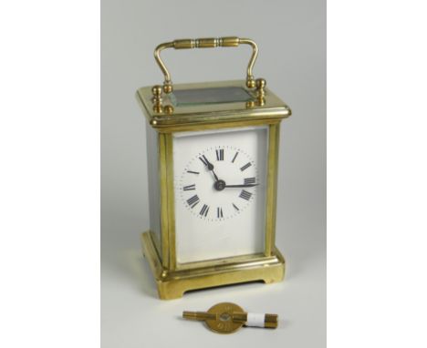 AN ENGLISH MADE BRASS CASED CARRIAGE CLOCK having a white enamel dial with Roman numerals, 15cms high including handle (key w