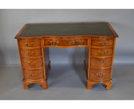 A Reproduction Yew Serpentine Twin Pedestal Desk the tall leather inset top above nine drawers with brass handles raised upon