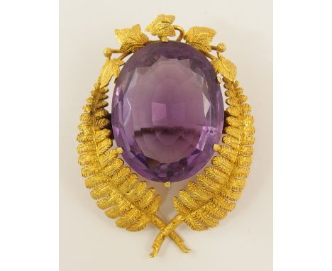 A bright yellow metal brooch designed as intertwined ferns and ivy leaves, circling a large facet cut amethyst, dimensions  4