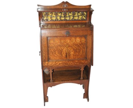 An Arts and Crafts oak, inlaid, stained and leaded glass writing desk with foliate copper and glass panel beneath a shelf and