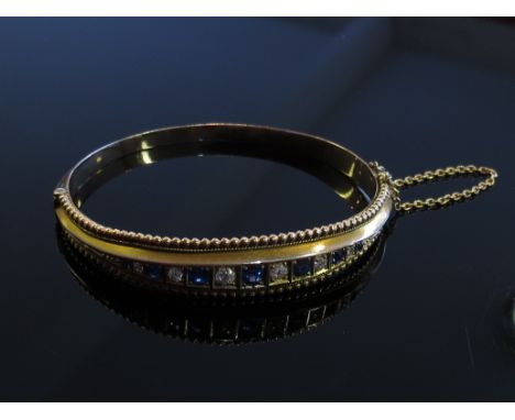 A gold stiff hinge bangle set with alternate diamonds and sapphires with safety chain, unmarked, 12.7g