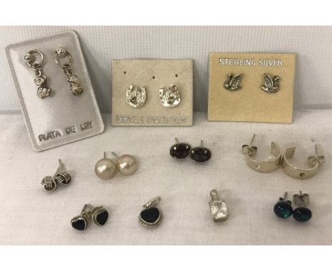 8 pairs of silver stud style earrings, to include a pair set with garnets. Together with a matching black enamel heart shaped