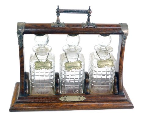 A late 19thC oak and plate mounted Tantalus, with three cut glass decanters and stoppers, each with plated decanter labels, w