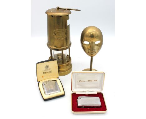 A vintage miners lamp, two 1960s cased cigarette lighters and brass mask on stand.