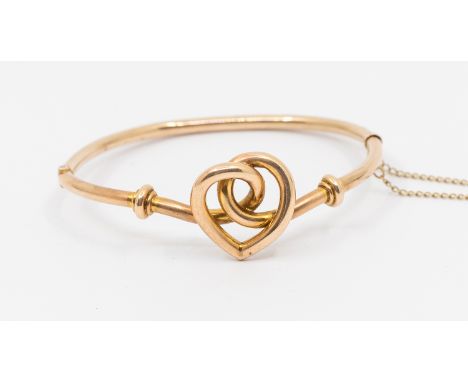 An early 20th century 9ct gold bangle, comprising a heart shaped detail to the front, width approx 22mm, to a hollow band wit