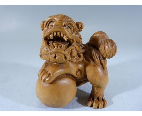 Japanese carved wooden Netsuke depicting a dragon with one foot astride a ball. 