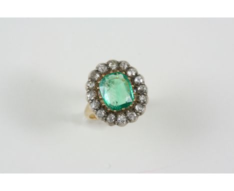 AN EARLY 20TH CENTURY EMERALD AND DIAMOND CLUSTER RING the rounded rectangular-shaped emerald is set within a surround of old