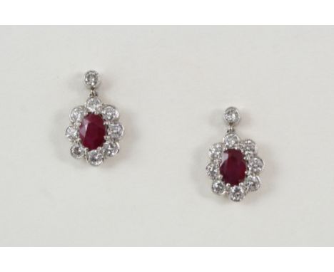 A PAIR OF RUBY AND DIAMOND CLUSTER DROP EARRINGS each set with an oval-shaped ruby within a surround of eight circular-cut di