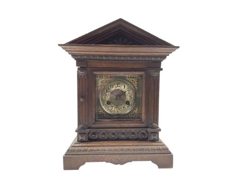 A German oak cased striking mantle clock with an architectural pediment, carved pilasters, shaped plinth and carved decoratio