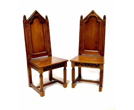 A pair of Gothic Revival oak dining chairs with ecclesiastical-style arched backs and carved finial decoration, on plank seat