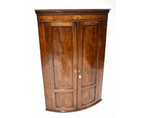 A 19th century mahogany bow-fronted corner cupboard, the cornice with dentil moulding over an inlaid frieze with fleur de lis