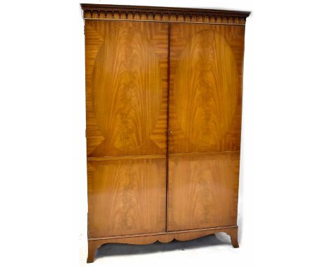 A Kendal Milne reproduction two-door wardrobe with a dentil moulded cornice above a pair of cupboard doors, on bracket feet, 