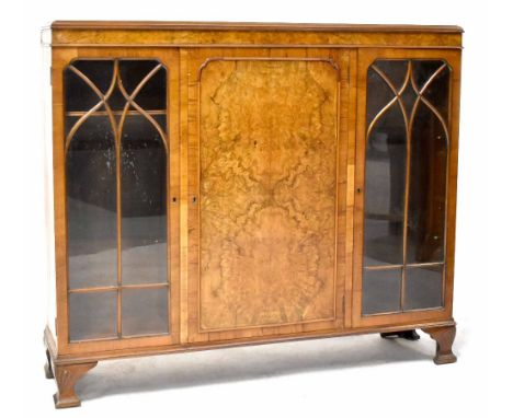 A mid-20th century walnut display cabinet, the central cupboard door flanked by a pair of astragal glazed doors, on carved br