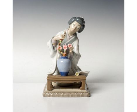 Beautiful glossy porcelain figurine of a geisha woman with a flower arrangement. This item has its original box which measure