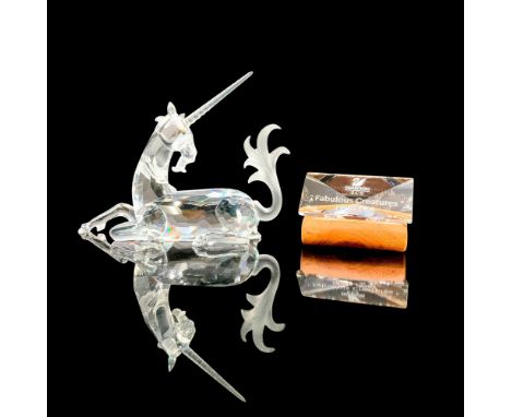 A clear crystal figure of a unicorn sitting down on all fours with its head slightly turned. Also included is its rectangular