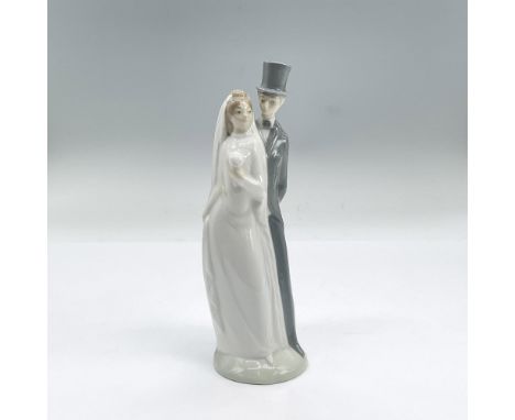 Glazed porcelain figural of a finely dressed couple on their wedding day. The groom wears a top hat and the bride holds her b