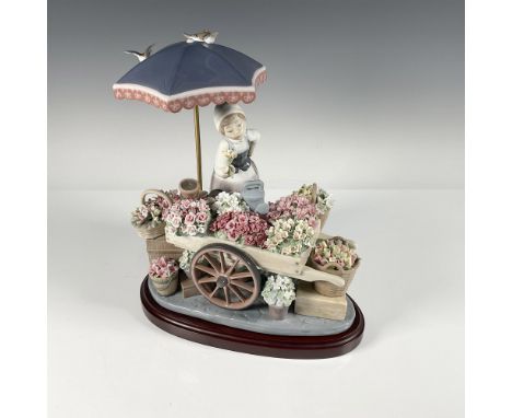 A figural work with young female flower seller figure with wheeled flower cart wagon, umbrella, birds, and a profusion of col