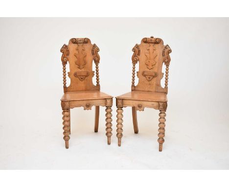 A pair of Victorian carved oak hall chairs, the backs with carved scroll and shield motifs between bobbin-turned side rails, 