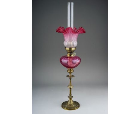 An early 20th century brass based oil lamp, with chimney, cranberry and opaque frilled and moulded shade, cranberry reservoir