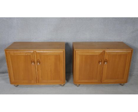 A pair of mid century vintage blonde elm Ercol Windsor cabinets, each with fitted interior on casters with maker's labels alo