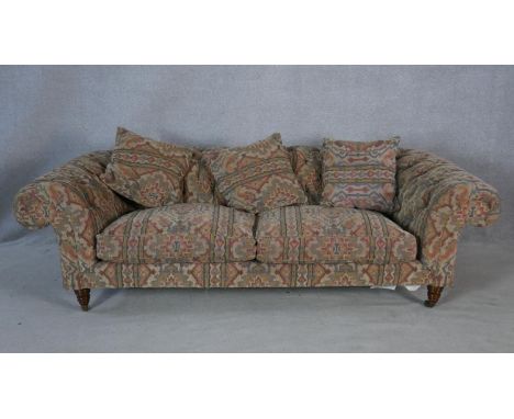 A Victorian style buttoned back Chesterfield sofa in tapestry style upholstery on turned tapering supports terminating in bra