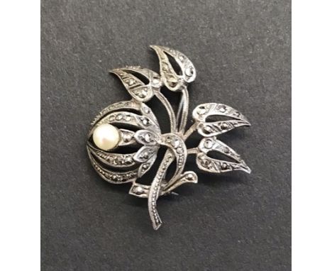 A Silver coloured brooch with white stones and pearl. Floral design brooch featuring a cultured pearl and marcasite 1950s/60s
