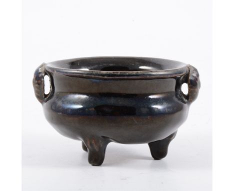 Chinese grey stoneware black glazed tripod censer, possibly Northern Song, rudimentary twin mask head handles, and raised on 