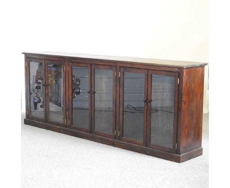 A large stained pine bookcase, with adjustable shelves, enclosed by six glazed doors, on a plinth base245w x 41d x 93h cmCond