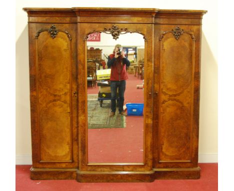 A Victorian figured walnut breakfront fitted wardrobe, having a moulded cornice and centre mirror door, flanked by arched pan